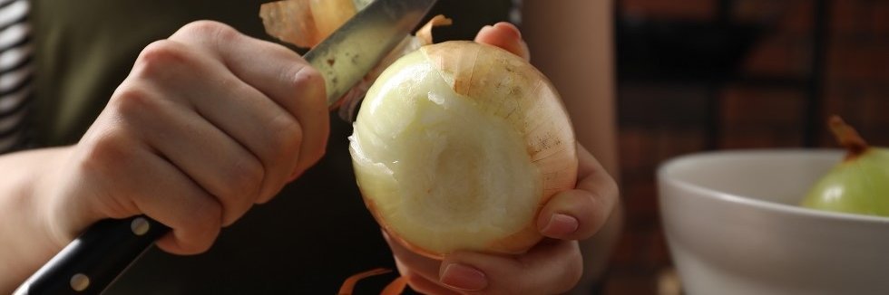 Eine Frau schält mit einem Küchenmesser eine große Zwiebel. 