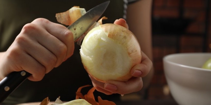 Eine Frau schält mit einem Küchenmesser eine große Zwiebel. . Artikel "Foodtrend „Onion Boil“" öffnen.