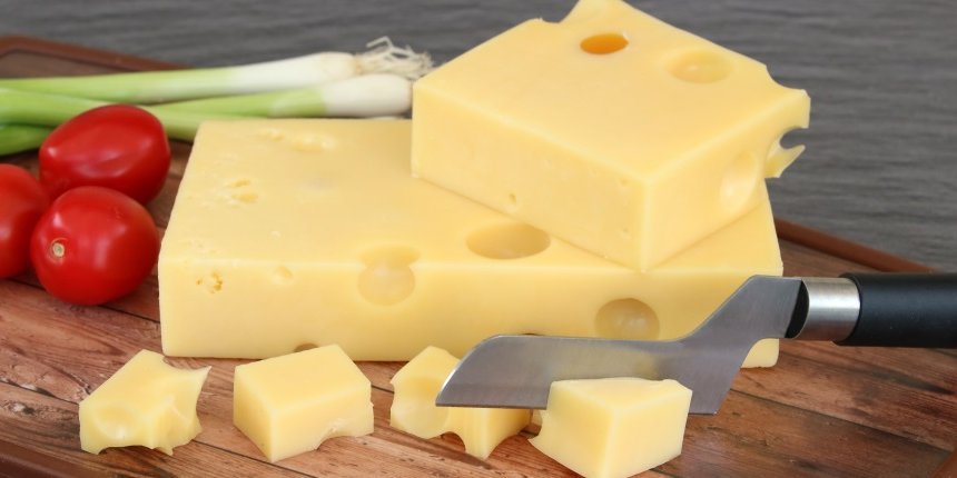 Auf einem Holzbrett liegen mehrere Stücke Emmentaler Käse neben Cocktailtomaten und Frühlingszwiebeln sowie einem Käsemesser.. Artikel "EU-Entscheid zum „Emmentaler“" öffnen.