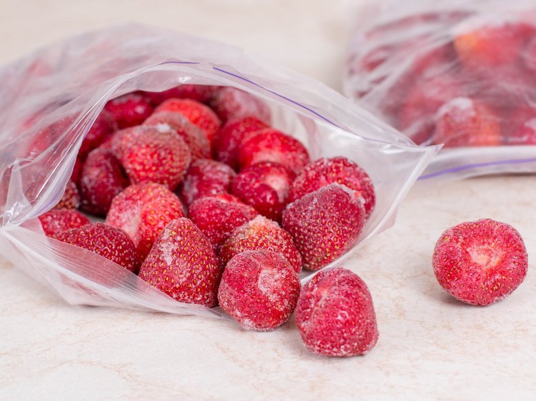 Einzelne, gefrorene Erdbeeren liegen in einer geöffneten Gefriertüte.