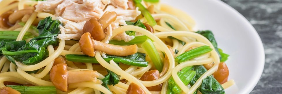 Auf einem weißen Teller liegt ein Nudelgericht mit Spaghetti, Pilzen und Spinatblättern.