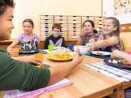 Schüler sitzen am Tisch im Klassenzimmer und essen selbst geschnippeltes Knabbergemüse.