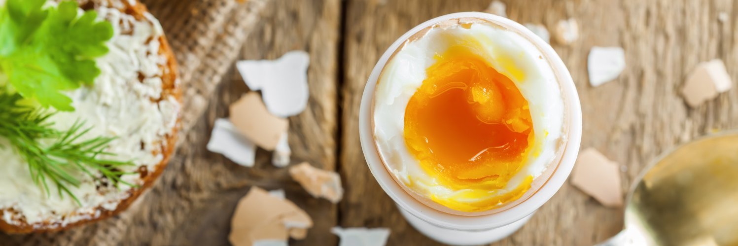 Wachsweich gekochtes Ei steht geöffnet inn einem Eierbecher auf einem Holztisch.