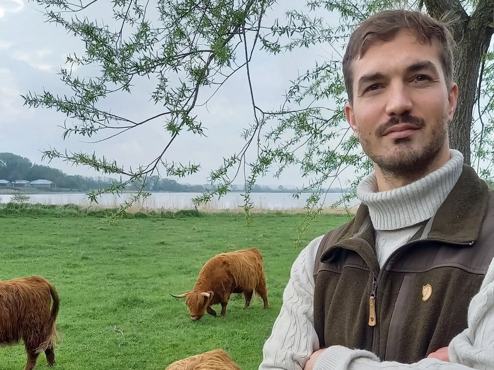 Ein Mann steht auf einer Weide. Daneben grasen Rinder.