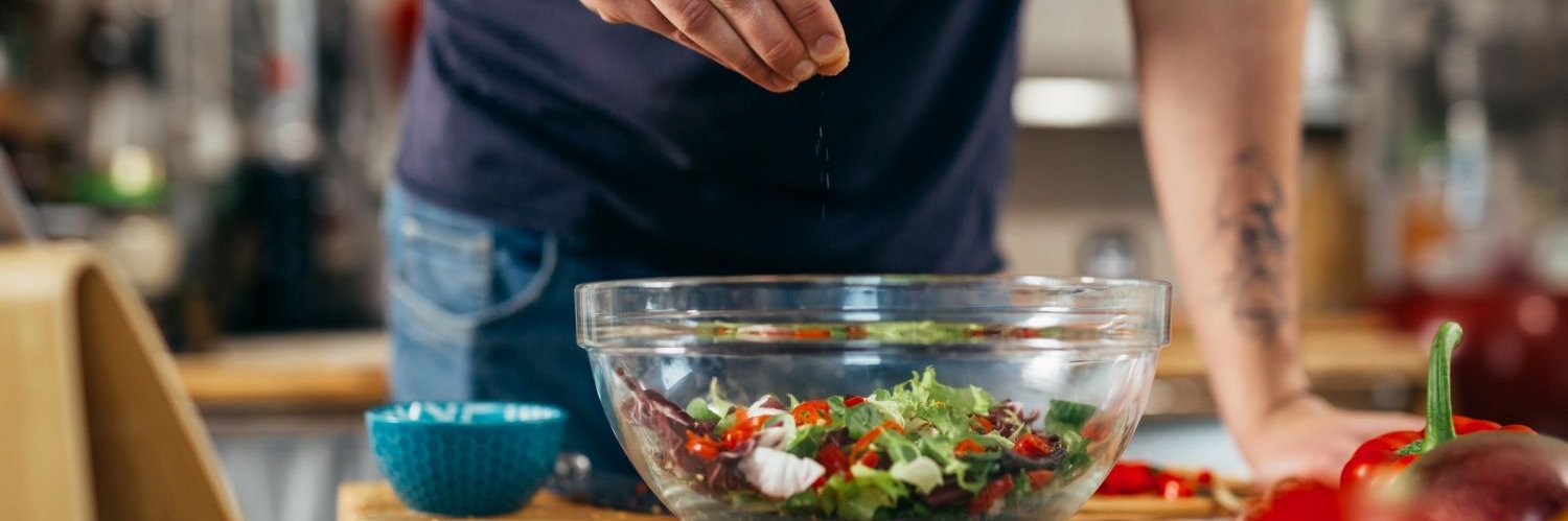 Mann streut mit einer Hand Salz über Salat.