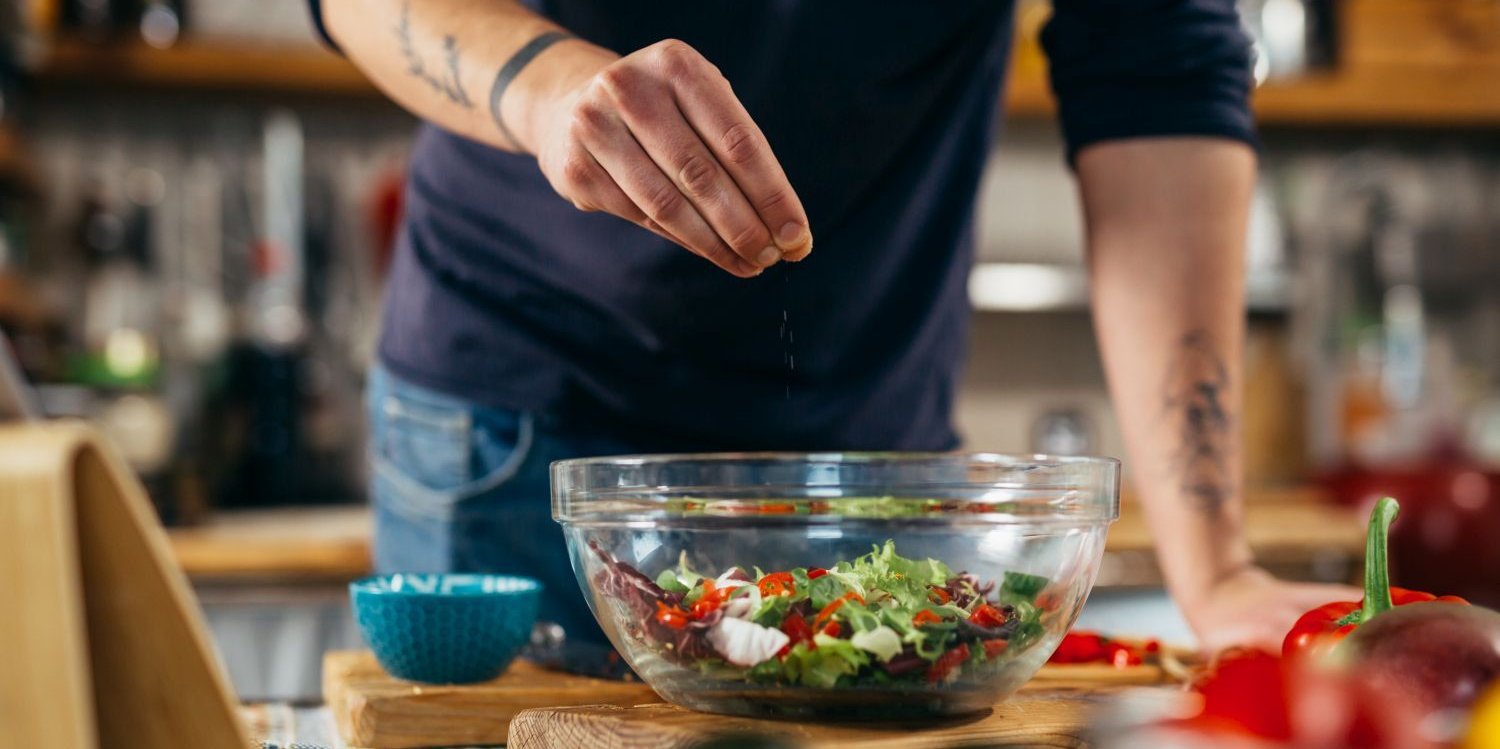 Mann streut mit einer Hand Salz über Salat.. Artikel "Wenn Salz, dann Jodsalz " öffnen.