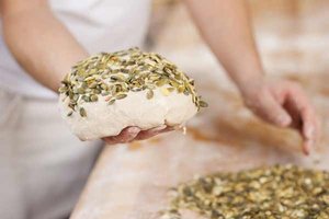 Bäcker hält Kürbiskernbrot-Rohling in der Hand