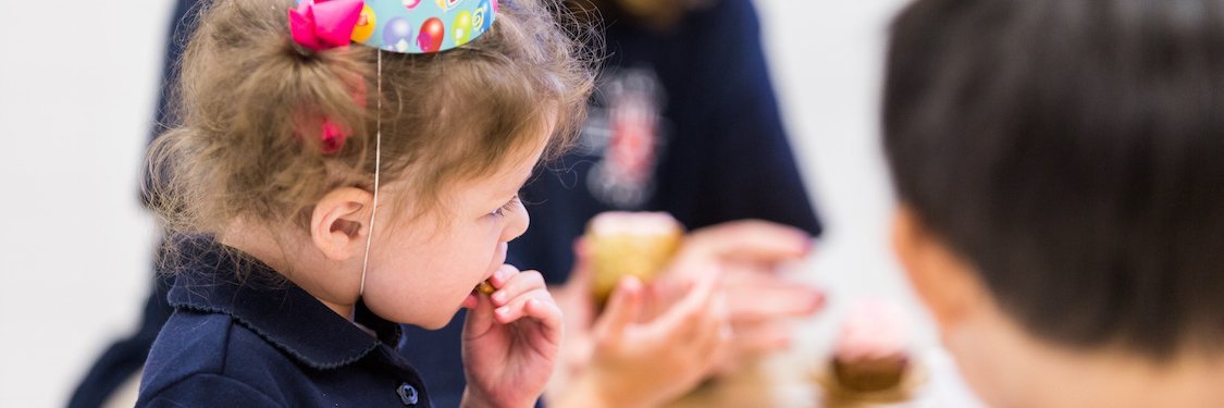 Ein Kleinkind mit Geburtstagshütchen isst einen süßen Muffin.