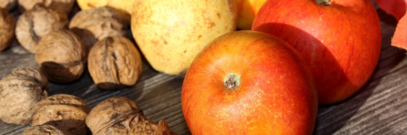 Äpfel, Walnüsse und Birnen liegen auf einem rustikalen Holztisch.