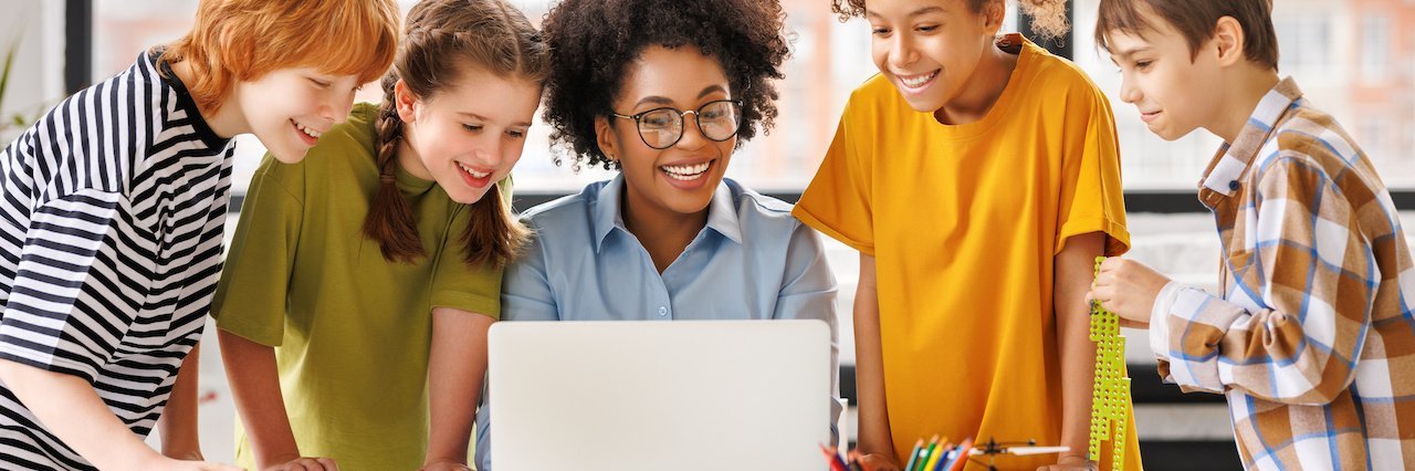 Fünf Schülerinnen und Schüler schauen gemeinsam auf einen Laptop.