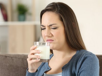 Eine Frau riecht an einem Glas mit Milch und rümpft die Nase.