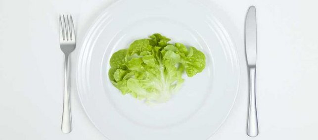 Salatblatt auf Teller, daneben Messer und Gabel