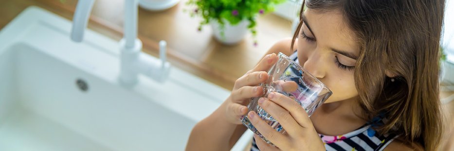 Mädchen trinkt Wasser aus einem Glas neben dem Wasserhahn