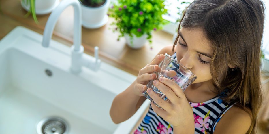 Mädchen trinkt Wasser aus einem Glas neben dem Wasserhahn. Artikel "Clevere Durstlöscher" öffnen.