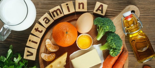 Verschiedene Vitamin-A-Reiche Lebensmittel liegen auf einem Tisch und zusätzlich liegen dort noch einzelne Buchstaben die das Wort Vitamin A bilden