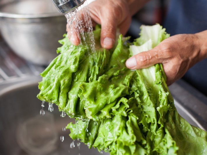 Hände waschen Salatblätter unter dem Wasserhahn.