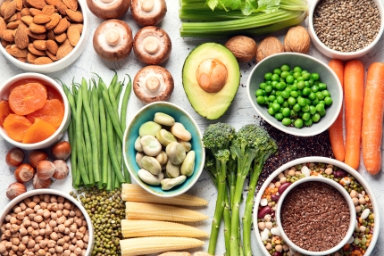 Tisch mit verschiedenen Lebensmitteln: Bohnen, Nüsse, Pilze, Brokkoli, Linsen, Trockenfrüchte, Mais und mehr