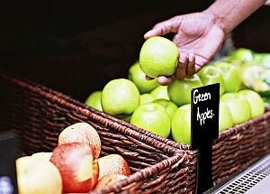 Hand hält grünen Apfel über Korb mit Äpfeln