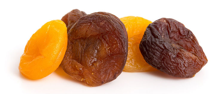 Fünf getrocknete Aprikosen vor weißem Hintergrund: zwei geschwefelte orangene und drei ungeschwefelte braune.