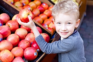 Junge hält an Stand mit Äpfeln Apfel in der Hand.