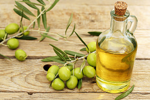 Fläschchen Olivenöl und im Hintergrund Olivenzweige