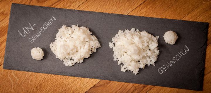 Zwei Haufen gekochter Reis auf einer Schieferplatte: links ungewaschen, rechts gewaschen vor dem Kochen.