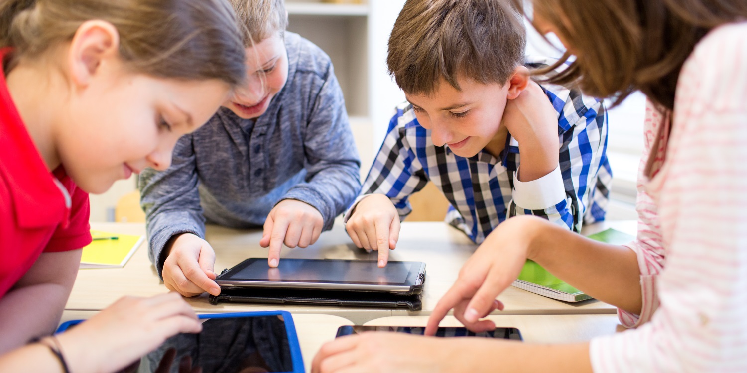 Zwei Mädchen und zwei Jungen beugen sich an einem Tisch über Tablets. . Artikel "Ist das schon Hunger oder noch Appetit?" öffnen.