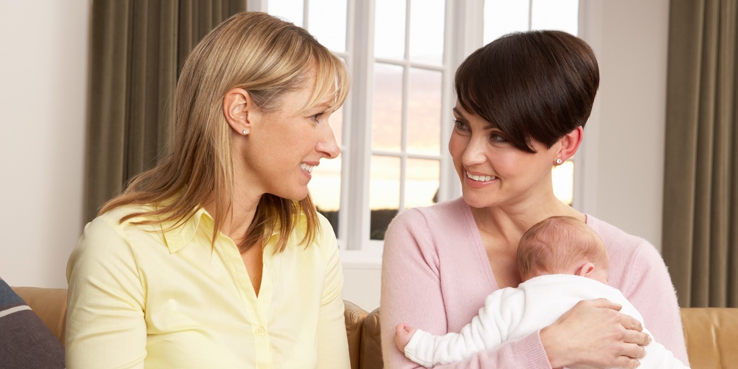 Eine blonde und eine dunkelhaarige Frau mit Säugling auf dem Arm sitzen einander zugewandt auf dem Sofa und unterhalten sich. . Artikel "Werbung zu Flaschennahrung ist streng geregelt " öffnen.