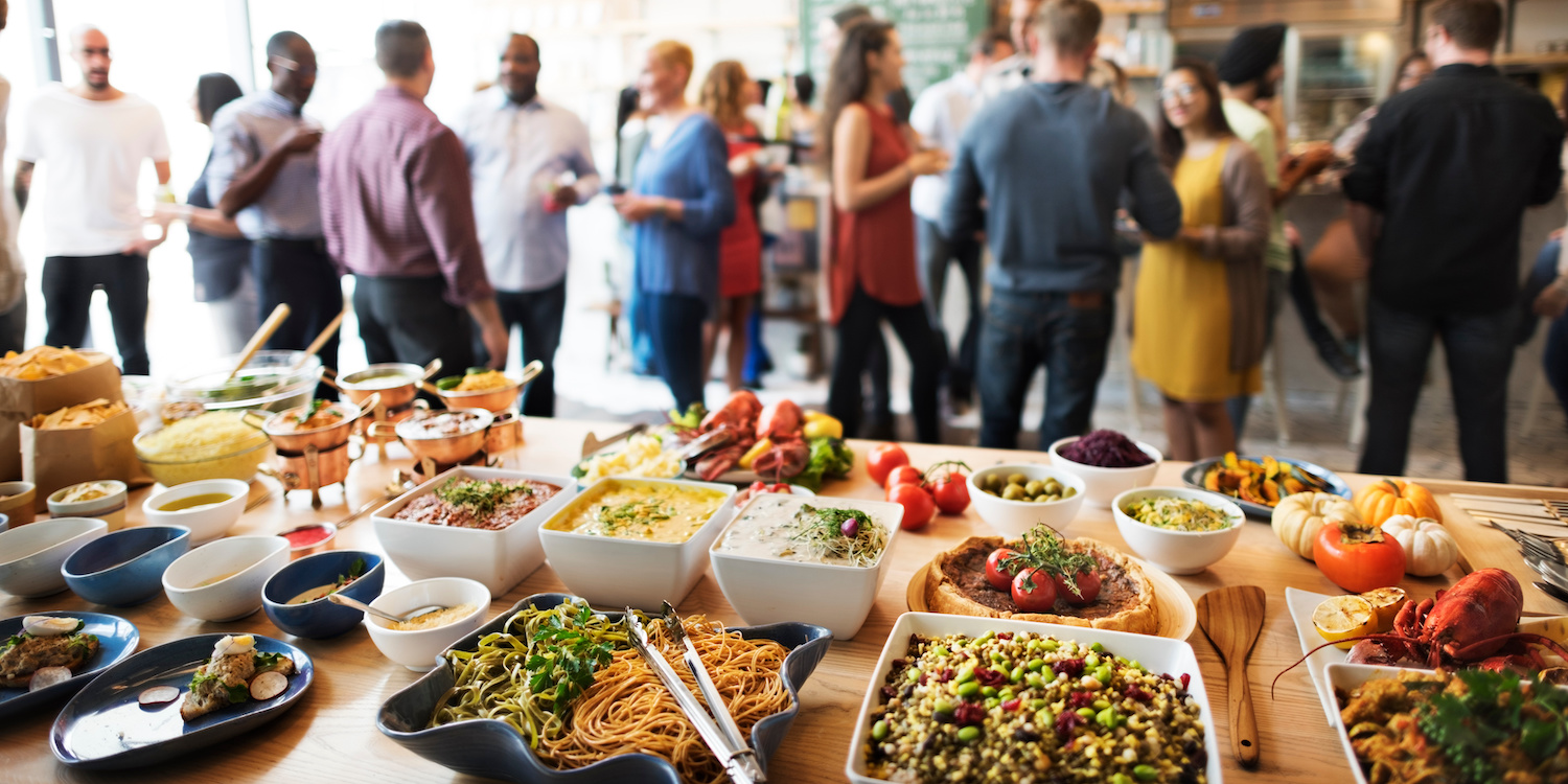 Im Vordergrund ist ein buntes, vegetarisches Buffet zu sehen, im Hintergrund unterhalten sich Menschen.. Artikel "Nachhaltiger essen auf Schulfesten" öffnen.